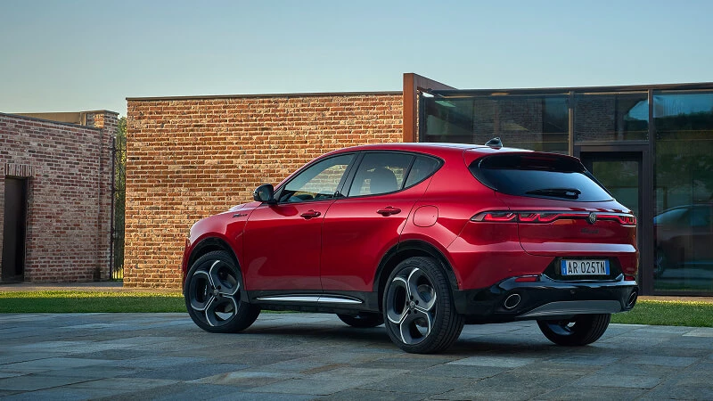 Červené Alfa Romeo Tonale pred tehlovou vilou pri západe slnka, zadný trojštvrťový pohľad