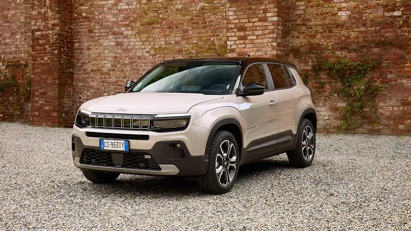 Béžový Jeep Avenger v elektrickej verzii pred tehlovou stenou – plne elektrické kompaktné SUV s uzavretou maskou a 54 kWh batériou