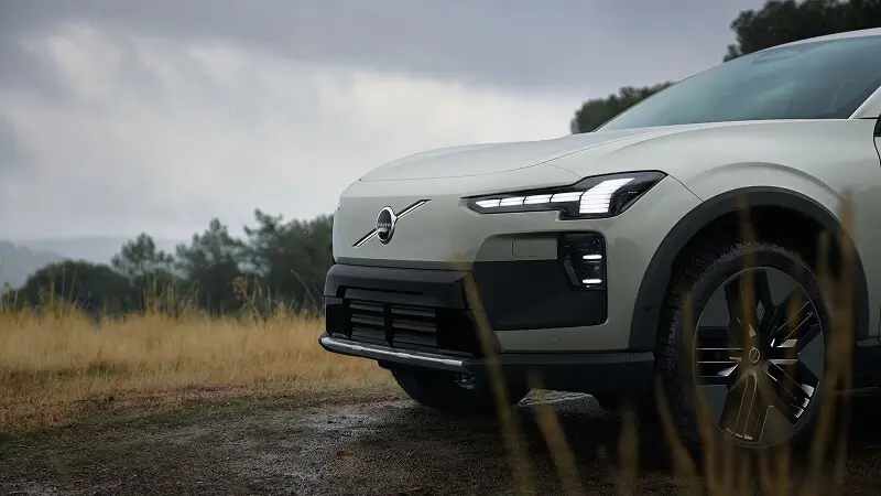 Detail prednej časti Volvo EX60 v zelenosivej farbe – LED svetlomety novej generácie a uzavretá maska typická pre elektromobil v outdoorovom prostredí