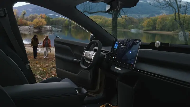 Interiér Volvo EX60 s vertikálnym dotykovým displejom a digitálnym kokpitom – pohľad cez čelné sklo na pár pri jesennom jazere