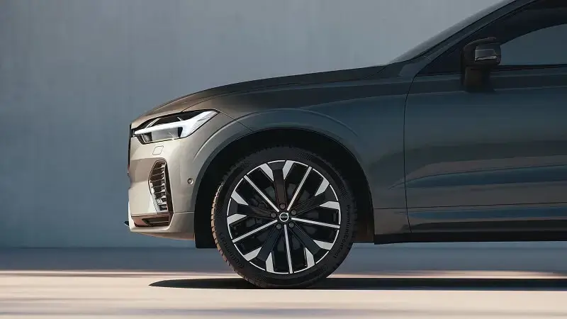 Detail predného kolesa a LED svetla Volvo XC60 v tmavosivej farbe pri betónovej stene