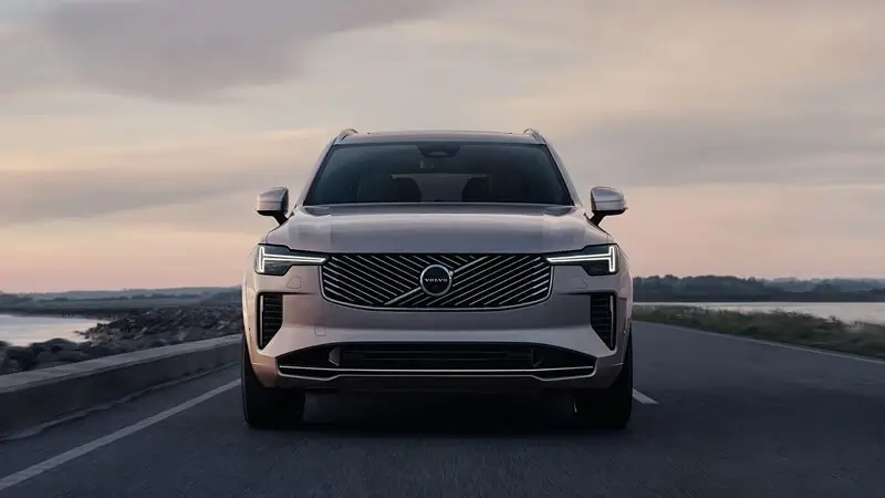 Predný pohľad na Volvo XC90 v sivej farbe na ceste pri mori – masívna chrómová maska s logom Volvo a LED svetlami v tvare Thorovho kladiva