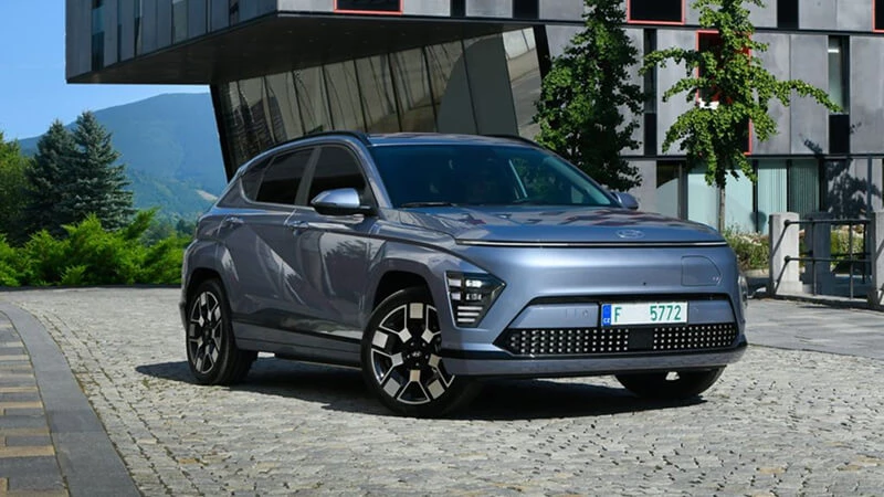 Svetlomodrý Hyundai Kona Electric zaparkovaný na dlažbe pred modernou budovou