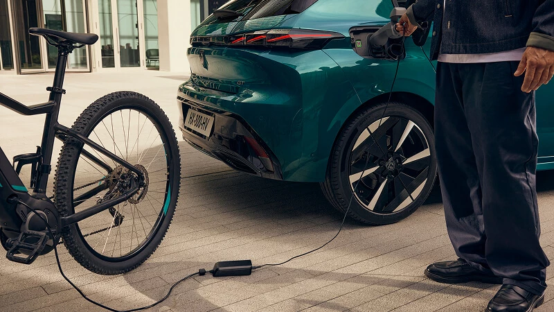 Nabíjanie Peugeot E-308 doma cez nabíjací kábel – zadná časť elektrického hatchbacku a e-bicykel